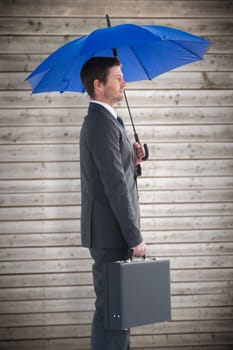 Serious businessman holding his umbrella and briefcase against wooden planks background