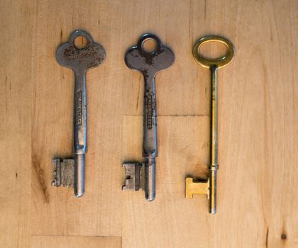 Two old rusty keys and one new on the wooden table