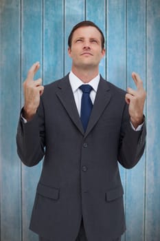 Serious businessman with fingers crossed is looking up against wooden planks