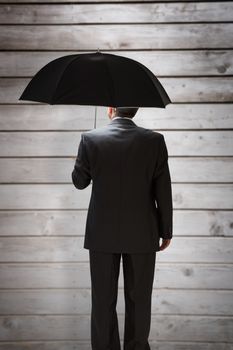 Mature businessman holding an umbrella against wooden planks