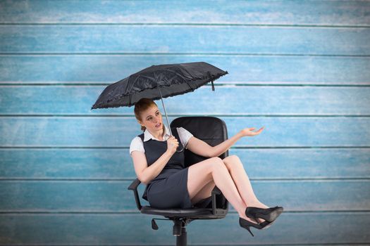 Businesswoman holding umbrella sitting on swivel chair against wooden planks