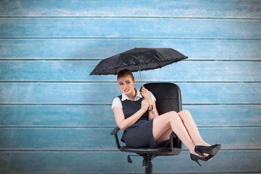 Businesswoman holding umbrella sitting on swivel chair against wooden planks