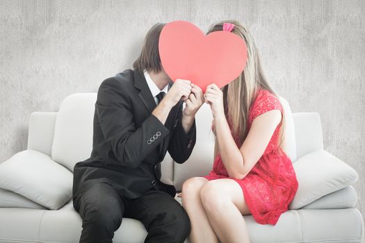 Cute geeky couple kissing and holding heart over faces against white background