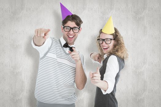 Happy geeky hispser couple dancing with party hat against white background