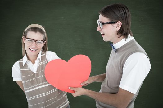 Geeky hipster offering red heart to his girlfriend  against green chalkboard