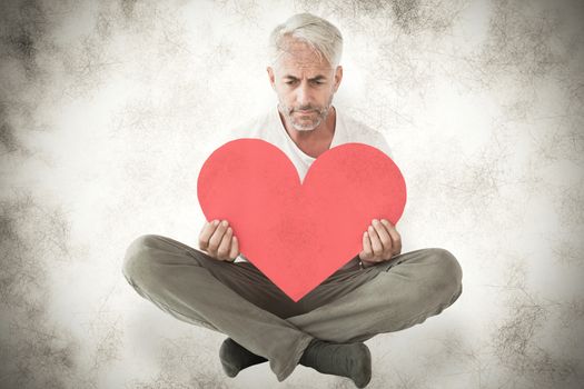 Upset man sitting holding heart shape against grey background