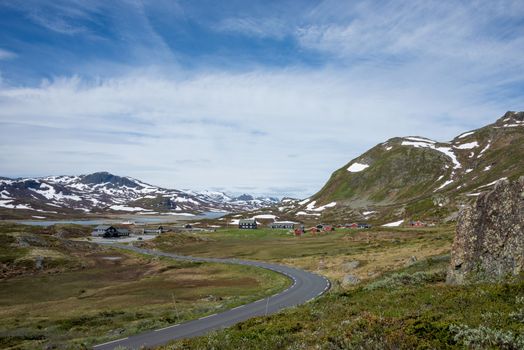Curvy road towards some wooden houses in a small remote village in a mountain landscape in Jotunheimen National Park, Norway.