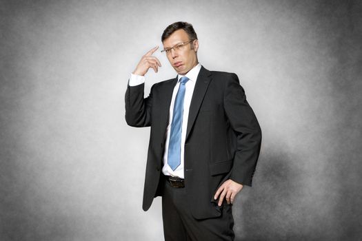 Image of conceited business man in dark suit pointing his finger to his head