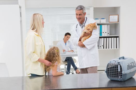 Veterinarian holding cat with its owners in medical office 