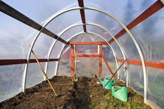 early spring time greenhouse inside construction with gardener tools and earth soil