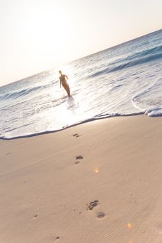 Happy woman enjoying in summer, running joyfully on tropical beach in sunset. Beautiful caucasian model wearing bikini on vacations on sandy beach. Footprints in sand. 