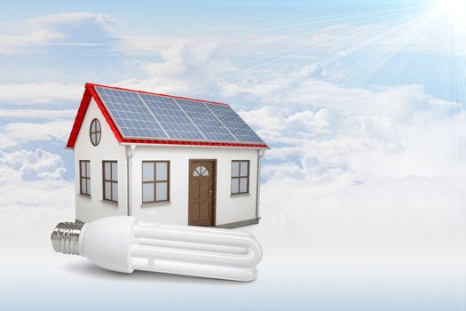 White house with red roof, brown door and solar panels in clouds. Background sun shines brightly on large clouds