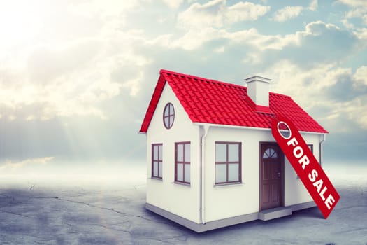 White house with label for sale, red roof, brown door and chimney. Background sun shines brightly on large clouds