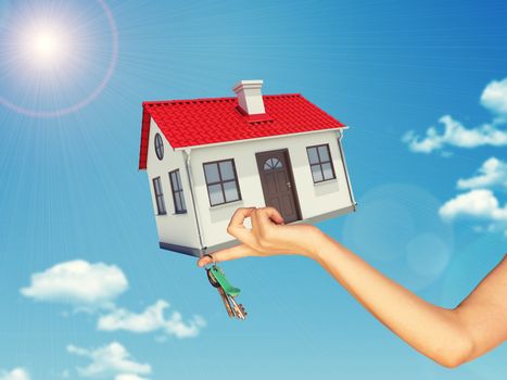 White house in hand with red roof, brown door and chimney. Background sun shines brightly. Blue sky