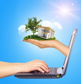White cottage in hand with green roof of screen laptop. Hands typing on keyboard. Background sun shines brightly on right. Blue sky