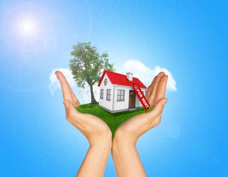 Hands holding house on green grass with label for rent, red roof, chimney, tree, wind turbine. Background clouds and blue sky