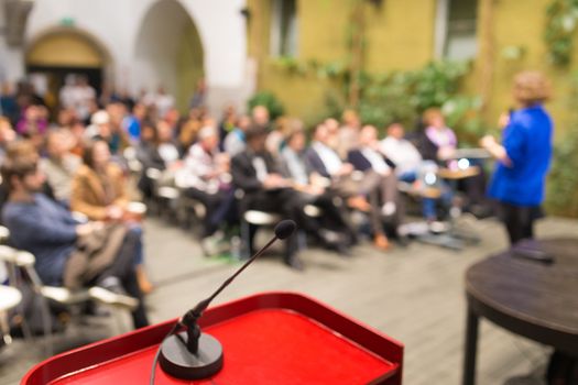 Female speaker at Business Conference. Audience at the conference hall. Business and Entrepreneurship. Business woman. Focus on microphone.