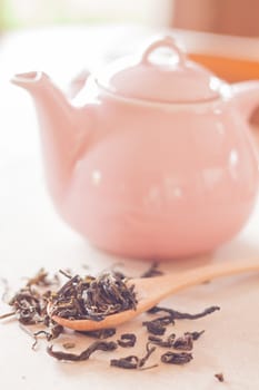 Dry tea in wooden spoon with ceramic jar, stock photo