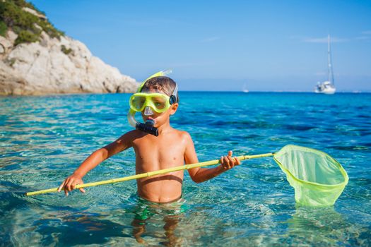Cute boy playing with scoop-net and swimming in the transparent sea