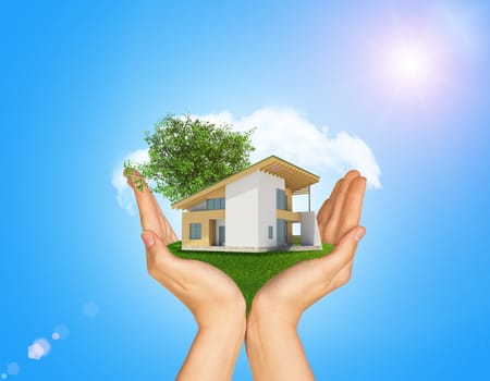 Hands holding cottage on green grass. Background of tree with leaves and cloud. Blue sky