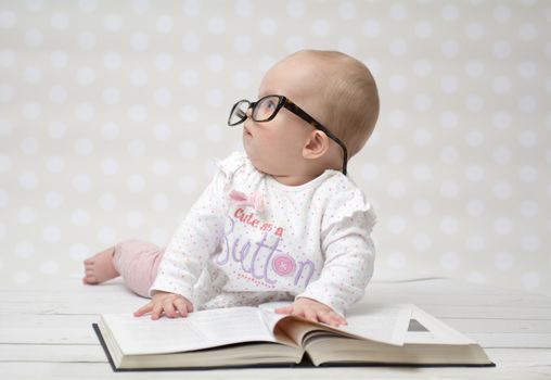 Funny portrait of a cute baby girl in glasses lying over a big book