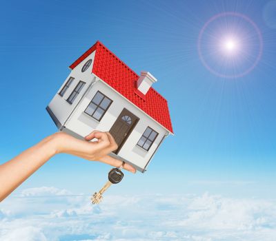 White house in hand with red roof, brown door and chimney. Background sun shines brightly. Blue sky