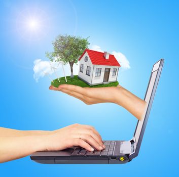 White shack in hand with red roof, brown door and chimney of screen laptop. Hands typing on keyboard. Hands typing on keyboard. Background sun shines brightly on left. Blue sky