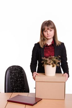 Woman fired from her job at the office, looking sadly into the frame with a box and a potted flower in hand