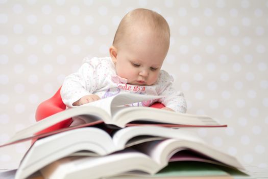 Cute baby girl reading behind a pile of books