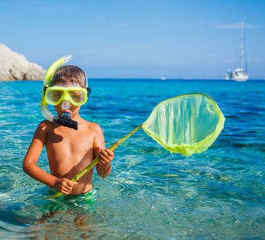 Cute boy playing with scoop-net and swimming in the transparent sea