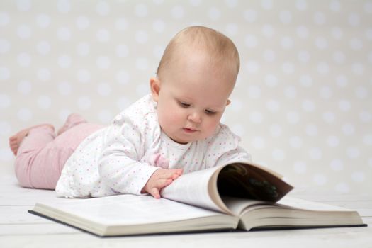 Baby girl lying on the belly reading a book