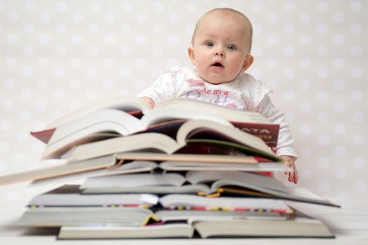 Cute baby girl sitting behind a pile of books