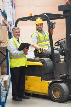 Driver operating forklift machine next to his manager in warehouse
