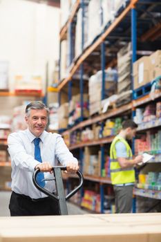 Manager pulling trolley with boxes in front of his employee in warehouse