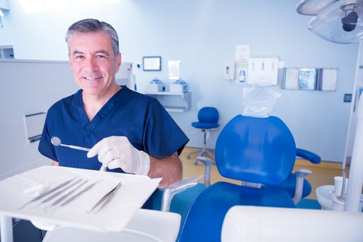 Dentist in blue scrubs smiling at camera holding tools at the dental clinic