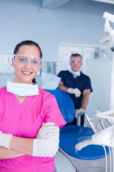 Smiling assistant and dentist behind her with protective glasses at the dental clinic