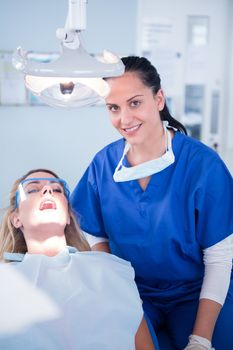 Dentist smiling at camera with patient in the chair at the dental clinic