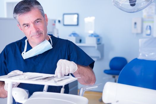 Dentist picking up tool and smiling at camera at the dental clinic