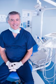 Smiling dentist in blue scrubs sitting in chair at the dental clinic