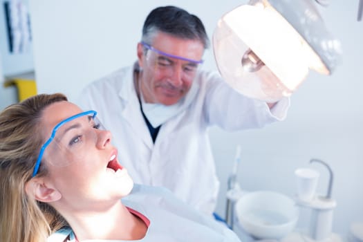 Dentist examining a patients teeth in chair under bright light at the dental clinic