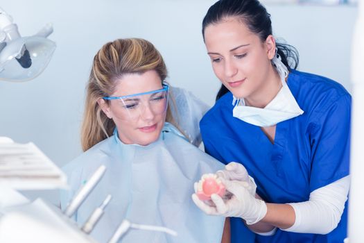 Dentist showing patient model of teeth at the dental clinic