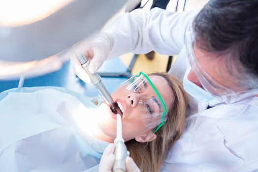 Dentist examining his patient with a suction hose at the dental clinic