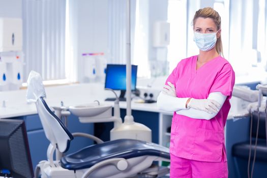 Dentist in surgical mask standing with arms crossed at dental clinic