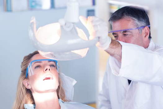 Dentist examining a patients teeth in chair under bright light at the dental clinic