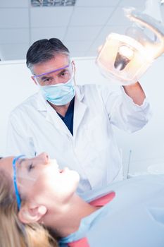 Dentist examining a patients teeth in chair under bright light at the dental clinic