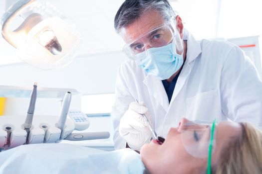 Dentist examining a patients teeth in the dentists chair at the dental clinic