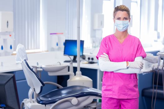 Dentist in surgical mask standing with arms crossed at dental clinic