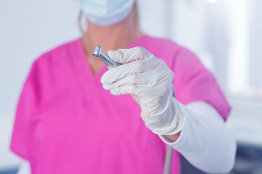 Dentist in surgical mask and scrubs holding tool at the dental clinic