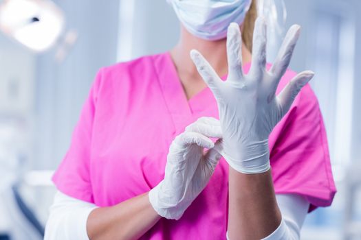 Dentist in pink scrubs putting on surgical gloves at the dental clinic