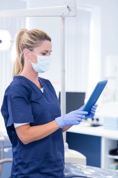 Dentist in mask and blue scrubs using her tablet at the dental clinic